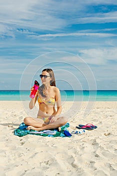 Young woman drinking sparkling water from transparent bottle on the beach, cancun