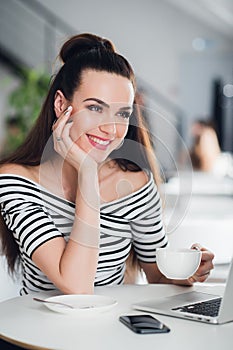 Young woman with drinking tea in a cafe. Beautiful adult woman with a cup of cappuccino at a cafe. Smiling brunette with