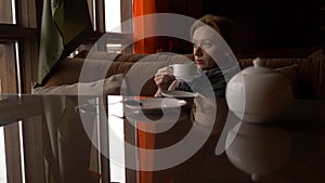 Young woman drinking tea in cafe near window with sea view. a woman in a scarf and sweater is drinking tea and basking