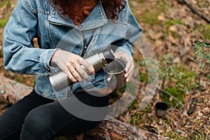 Young woman drinking tea in cup. Woman pours a drink into a mug from a thermos. Girl drinking tea while hike