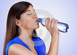 Young woman drinking water from bottle on blue background