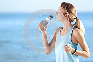 Young woman drinking water from bottle after fitness exercises on beach