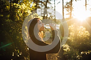 Young woman drinking water from bottle in nature.Bottled water.Hydration.Water intake for healthy body and skin.Natural mineral