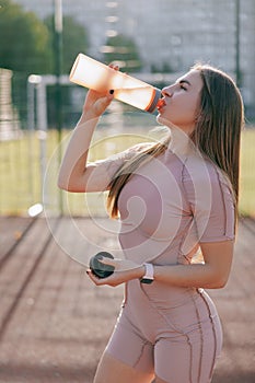 Young woman drinking water from bottle after training on the sports ground