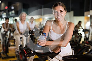 Young woman drinking water during cycling class in gym