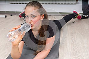 Young woman drinking water while lying on gym mat
