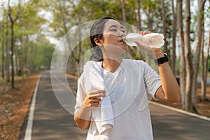 Young woman drinking water from a plastic bottle after her morning run at a local running park