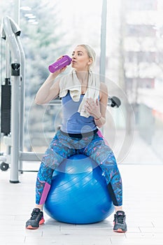 Young woman drinking water and taking a break after workout in g