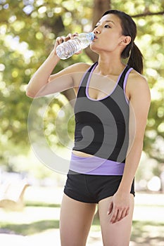 Young Woman Drinking Water Whilst Exercising In Park