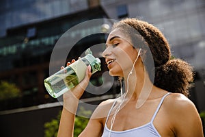 Young woman drinking water after workout outdoors at street