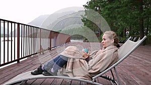 Young woman drinks hot coffee or tea near mountain river. Calm and cozy time in mountain resort.