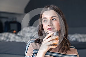 A young woman drinks juice while sitting in the room.