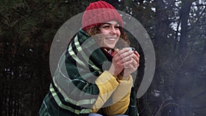 Young woman drinks tea by the fire in the winter forest