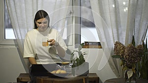 Young woman drinks tea and looks at tablet in cafe. Media. Student watches video on break and drinks tea in cozy cafe