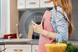 Young woman drinks tea while standing in kitchen