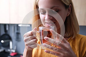 Young woman drinks tea from transparent cup closeup
