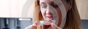 Young woman drinks tea from transparent cup closeup