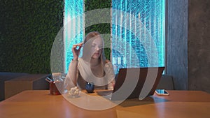 Young woman drinks tea and works on notebook in cafe