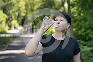 Young woman drinks water while jogging in the park. Drinking regime during sports