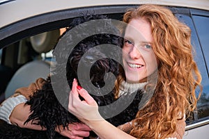 Young woman driver with black puppy poodle dog sitting in car.