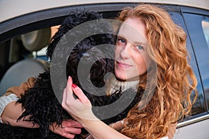 Young woman driver with black puppy poodle dog sitting in car.