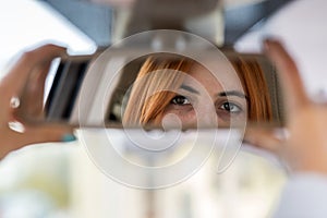 Young woman driver checking rear view mirror looking backwards while driving a car