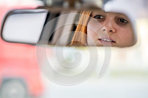 Young woman driver checking rear view mirror looking backwards while driving a car