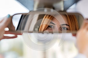 Young woman driver checking rear view mirror looking backwards while driving a car