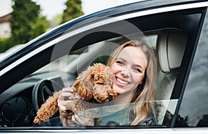 Young woman driver with a dog sitting in car, looking out of window.
