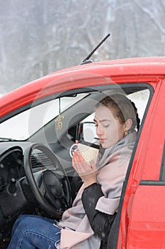 Young woman driver drinks hot tea from mug in  red car. Travel break concept