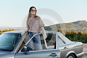 A young woman driver looks out of the car at the autumn landscape and smiles satisfactorily