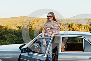 A young woman driver looks out of the car at the autumn landscape and smiles satisfactorily