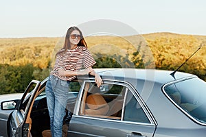 A young woman driver looks out of the car at the autumn landscape and smiles satisfactorily