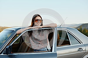 A young woman driver looks out of the car at the autumn landscape and smiles satisfactorily
