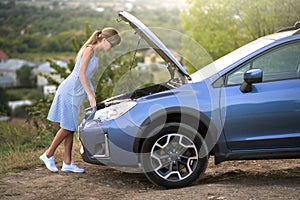 Young woman driver standing near a broken car with open hood having trouble with her vehicle