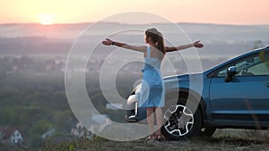 Young woman driver standing near a broken car with open hood having trouble with her vehicle.