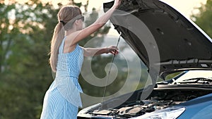Young woman driver standing near a broken car with popped up hood waiting for help to arrive.