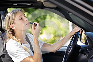 young woman in drivers seat car applying lipstick