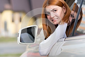 Young woman driving a car backwards. Girl with funny expression on her face while she made a fender bender damage to a rear