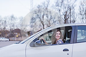 Young woman driving a car in the city. Portrait of a beautiful woman in a car, looking out of the window and smiling. Travel and