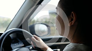 Young woman driving a car, hand put on the black steering wheel and looking forward with determination.