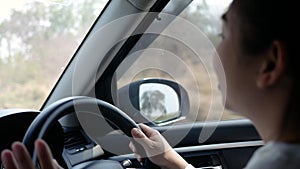 Young woman driving a car, hand put on the black steering wheel and looking forward with determination.