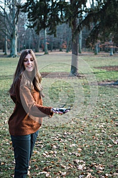 Young woman with a drone perched on her hand and a green park in background