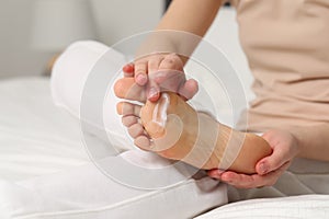 Young woman with dry skin applying cream onto her foot indoors, closeup