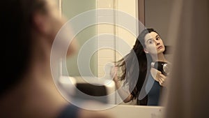 Young woman drying her hair with dryer in front of the mirror