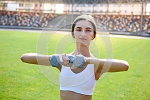 Young woman with dumbells posing outside. She`s making morning exercises outdoors