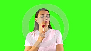 Young woman eagerly sucks a lollipop. Green background people sincere emotions concept of sweet tooth