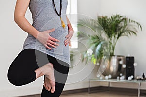 Young woman in early pregnancy doing tree pose holding belly
