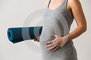 Young woman in early pregnancy with rolled mat under her arm going to prenatal yoga class