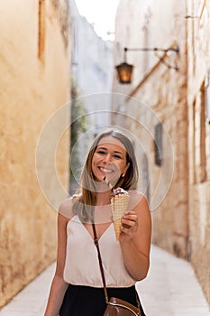 Young woman eat ice cream in a narrow alley in Mdina, Malta